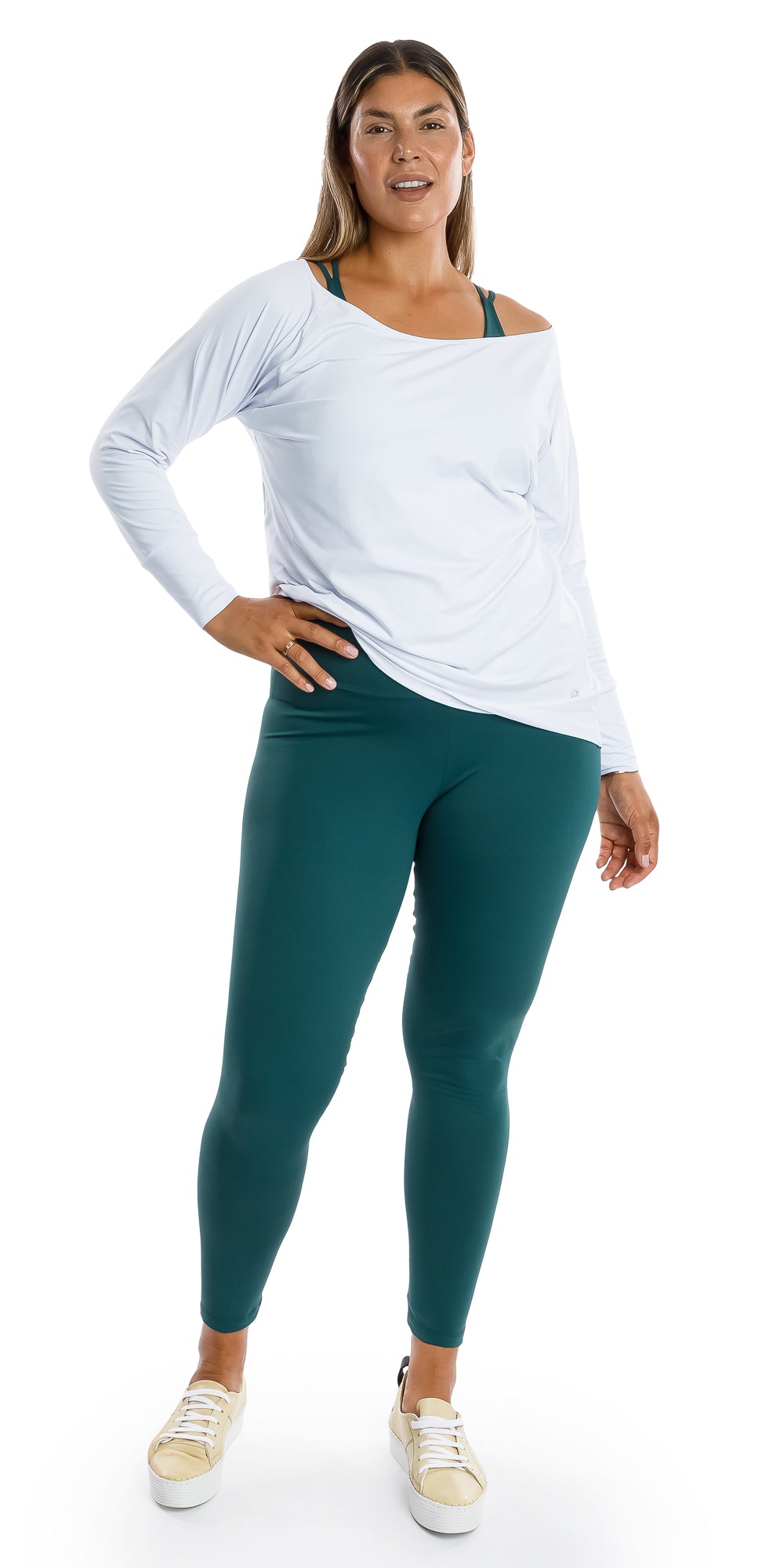 Full body front view of lady in White Off The Shoulder Long Sleeve Tee and teal coloured leggings leaning on left leg and putting right hand on waist