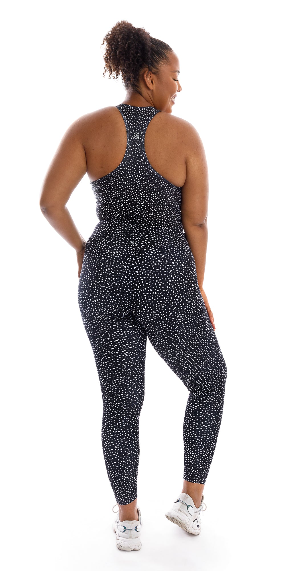 Full body rear view of girl wearing black Star Dust Body Luxe Ultra High Waist Leggings and white shoes looking over right shoulder and lifting right heel while putting left hand on waist