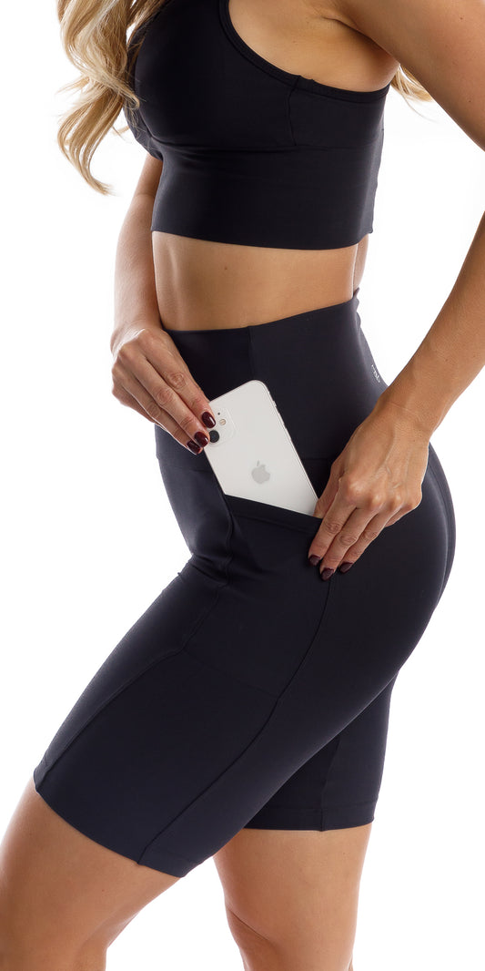 Side view of girl in black Midnight Eco Biker Shorts with Pockets putting phone in the pocket
