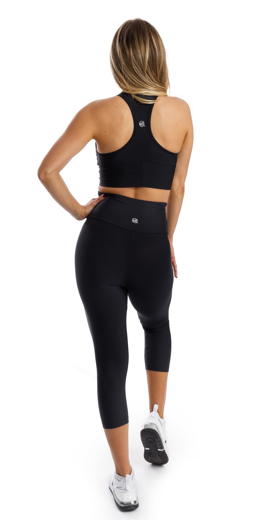 Full body rear view of girl in black Midnight Eco Capri Leggings and matching racer back bra putting one hand on waist