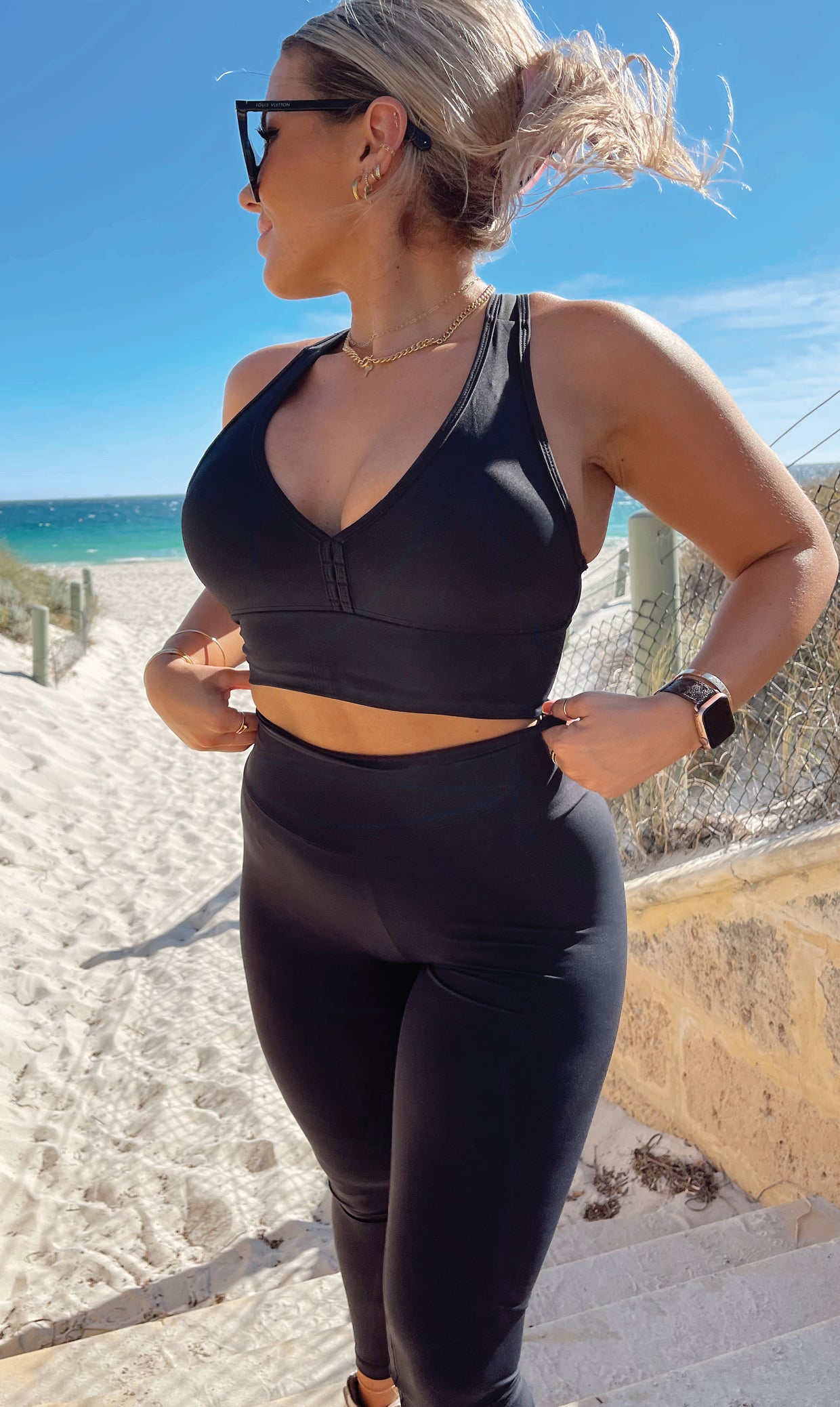 Front view of girl in black Midnight Body Luxe Scrunch Bum Leggings and matching bra putting both hands at the end of the bra and looking to her right