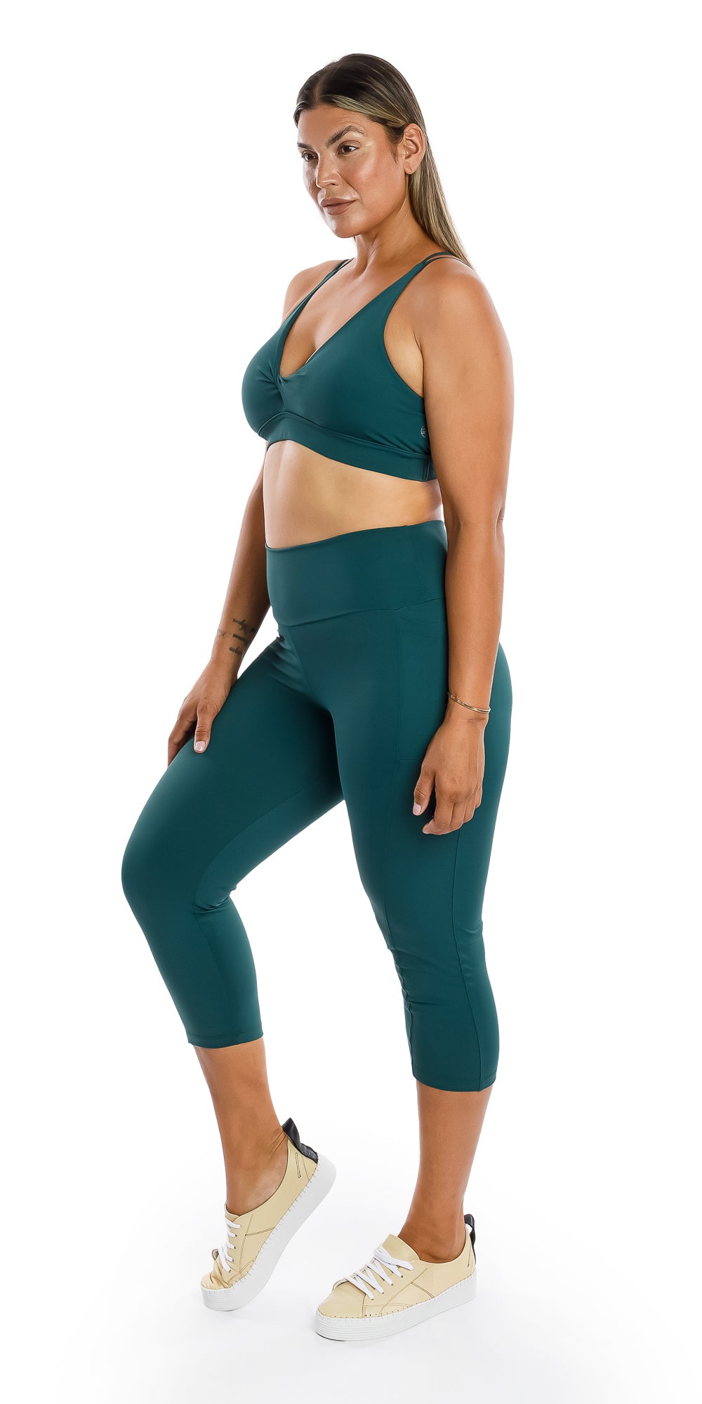 Full body angled side to front view of lady in coloured Teal Body Luxe Diamond Back Bra and matching bottoms putting right foot forward while lifting its heel and putting hand on lap