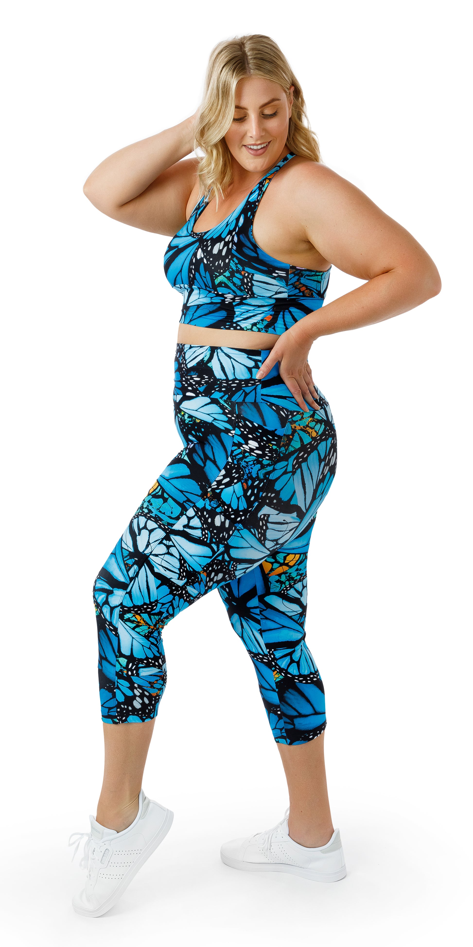 Full body side view of girl in blue animal print JH Butterfly Eco Capri Leggings with Pockets and matching bra putting one hand on her head and the other on her waist
