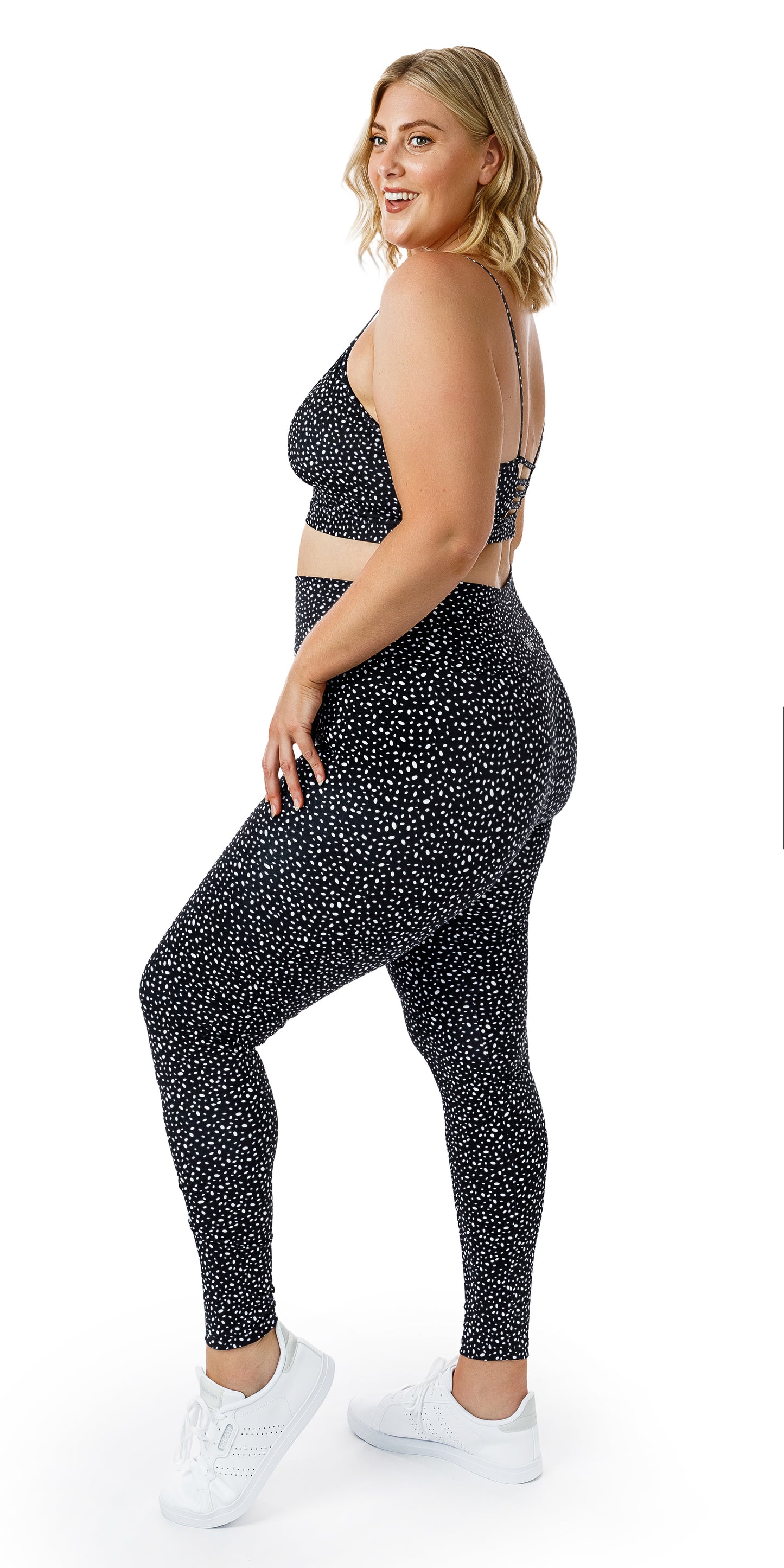 Full body side view of lady in black Star Dust Momentum Bra and matching leggings putting left foot forward lifting its heel and putting left hand on lap
