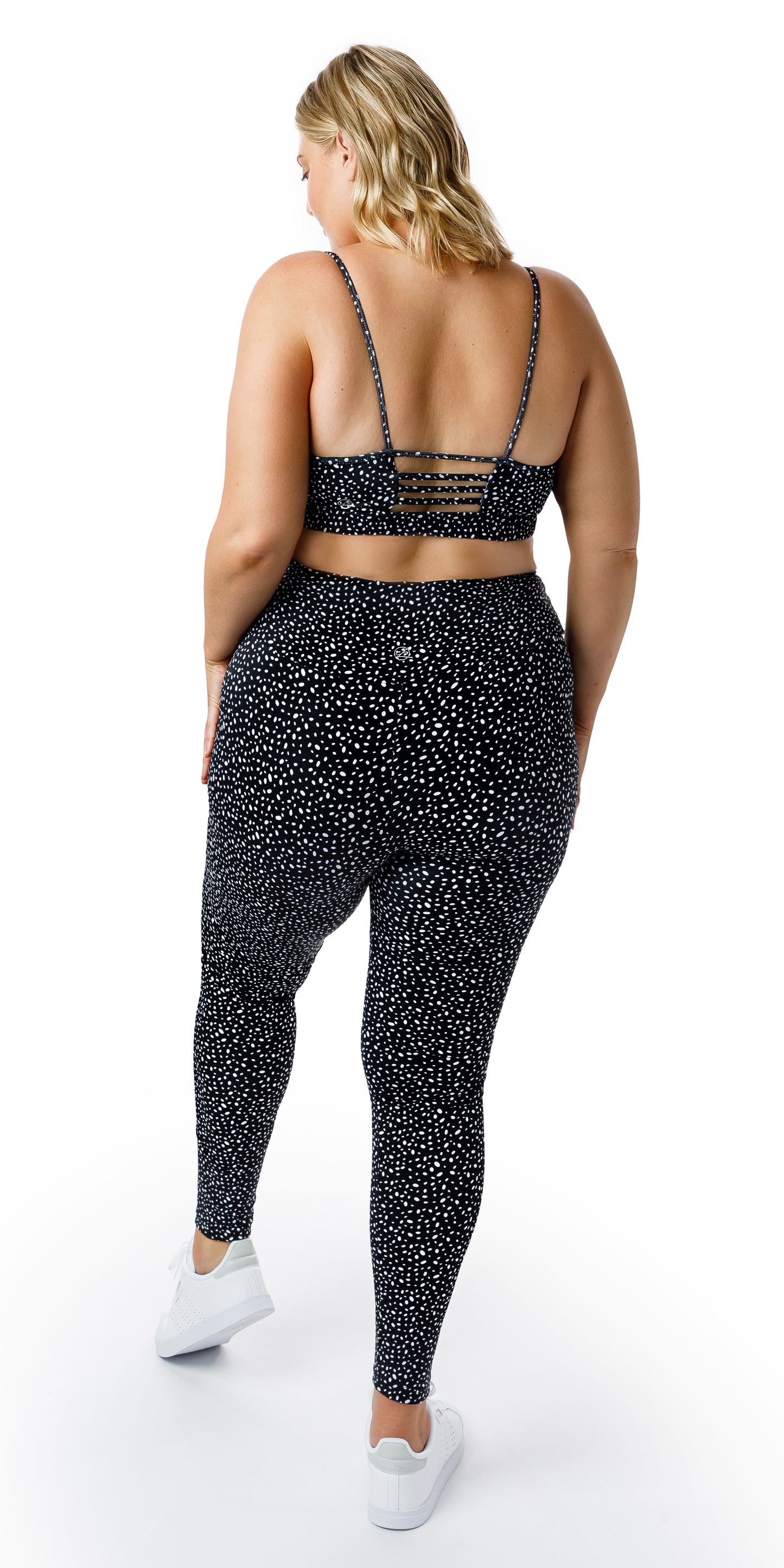 Full body back view of lady in black Star Dust Momentum Bra and matching leggings putting left foot forward and hand on lap