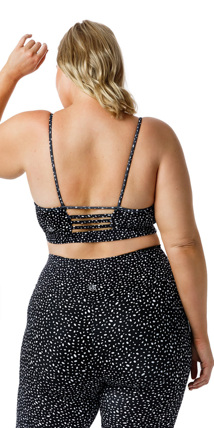 Back view of lady in black Star Dust Momentum Bra and matching bottoms raising left arm while resting the other