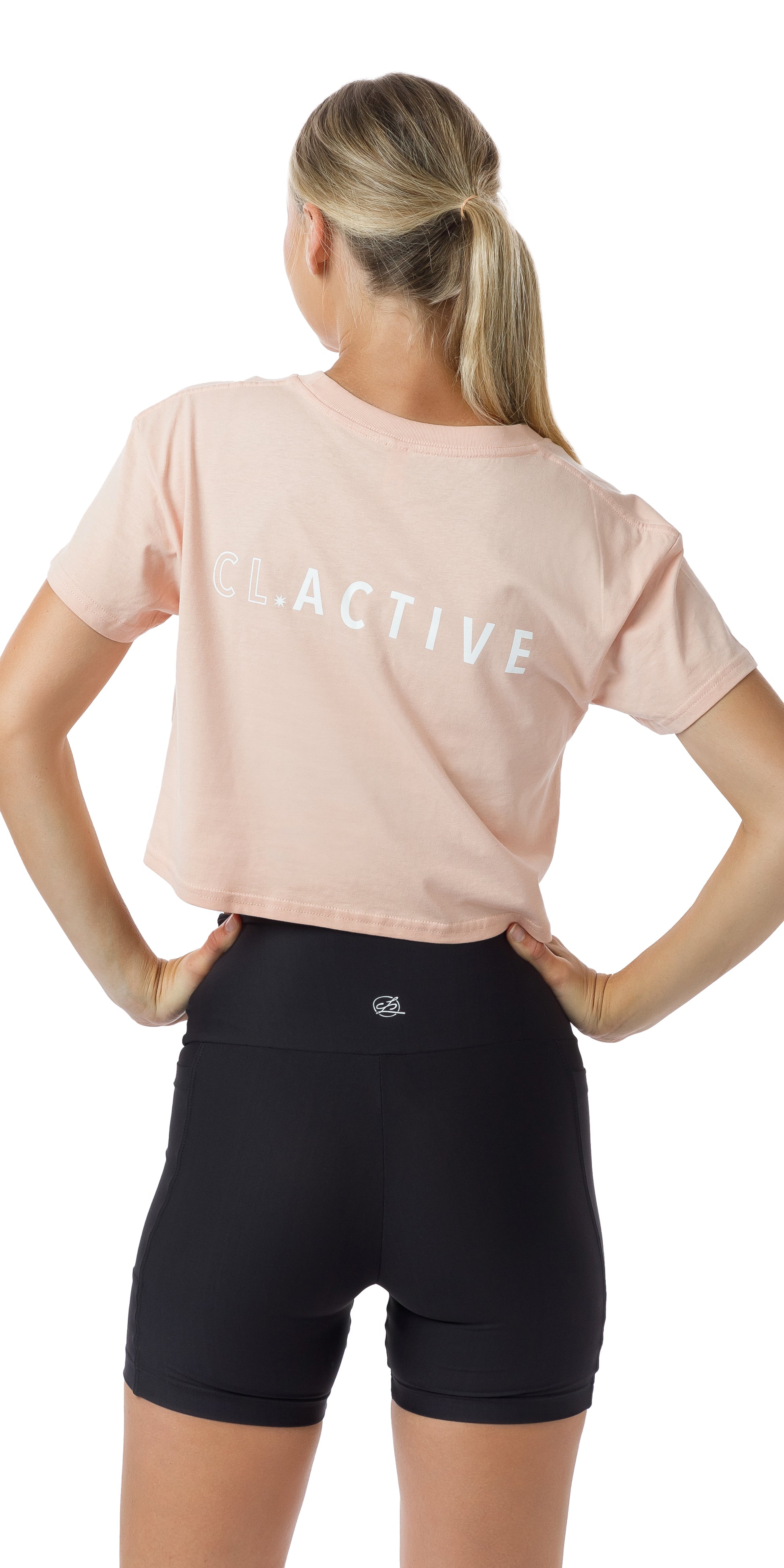 Rear view of girl in Pink CL Active Crop Tee and black biker shorts putting both hands on waist