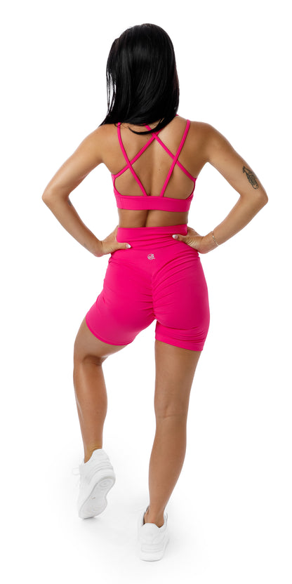 Full body rear view of girl wearing pink strappy sports bra and matching Candy Body Luxe Scrunch Bum Midi Shorts