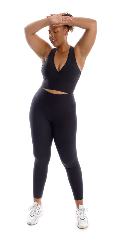 Full body front view of girl wearing black Midnight Eco Racer Back Bra and matching leggings putting both hands on forehead facing outward