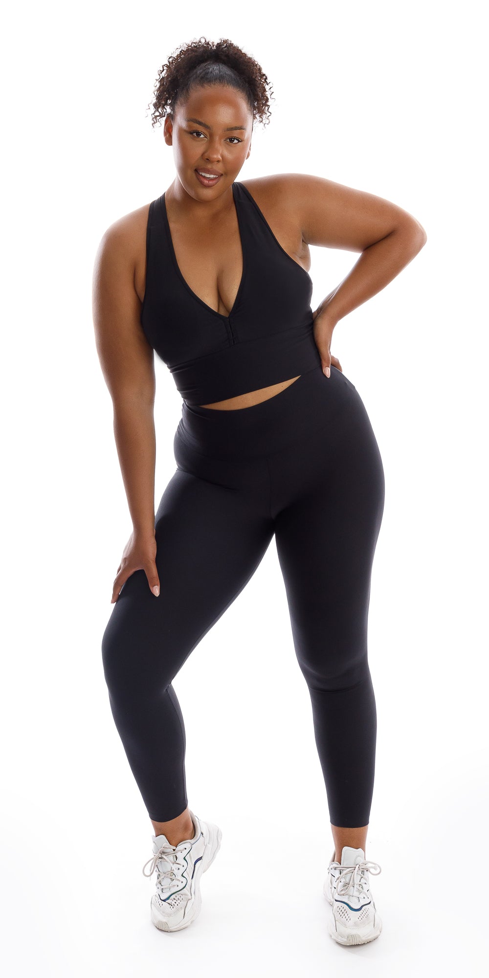 Full body front view of girl wearing black Midnight Eco Racer Back Bra and matching leggings putting one hand on waist and bending her right knee