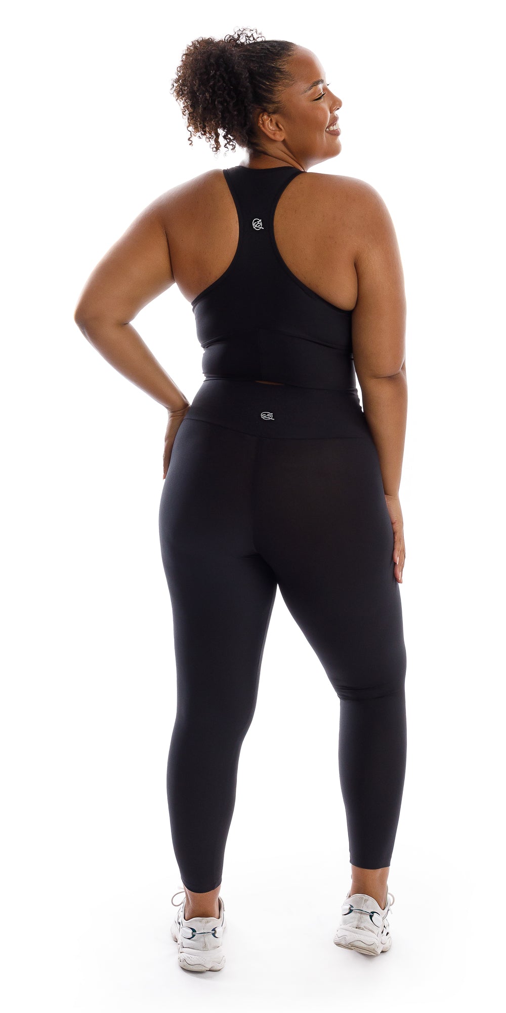 Full body rear view of girl wearing black Midnight Eco Racer Back Bra and matching leggings putting one hand on waist