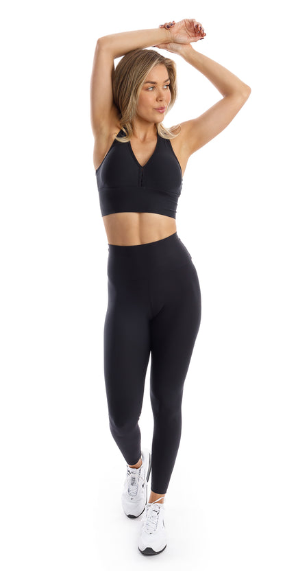 Full body front view of girl wearing black Midnight Eco Ultra High Waist Leggings and matching bra lifting both arms towards the top of her head