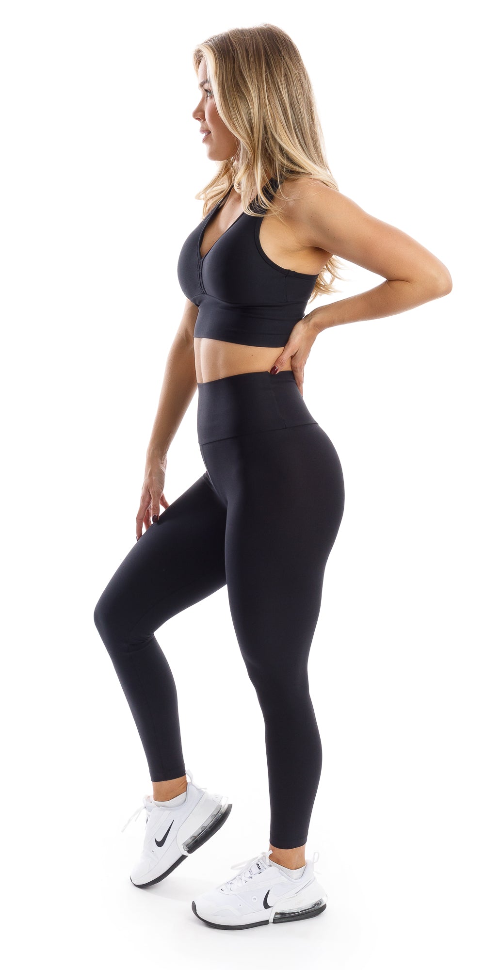 Full body side view of girl wearing black Midnight Eco Ultra High Waist Leggings and matching bra lifting right heel and putting left hand on waist