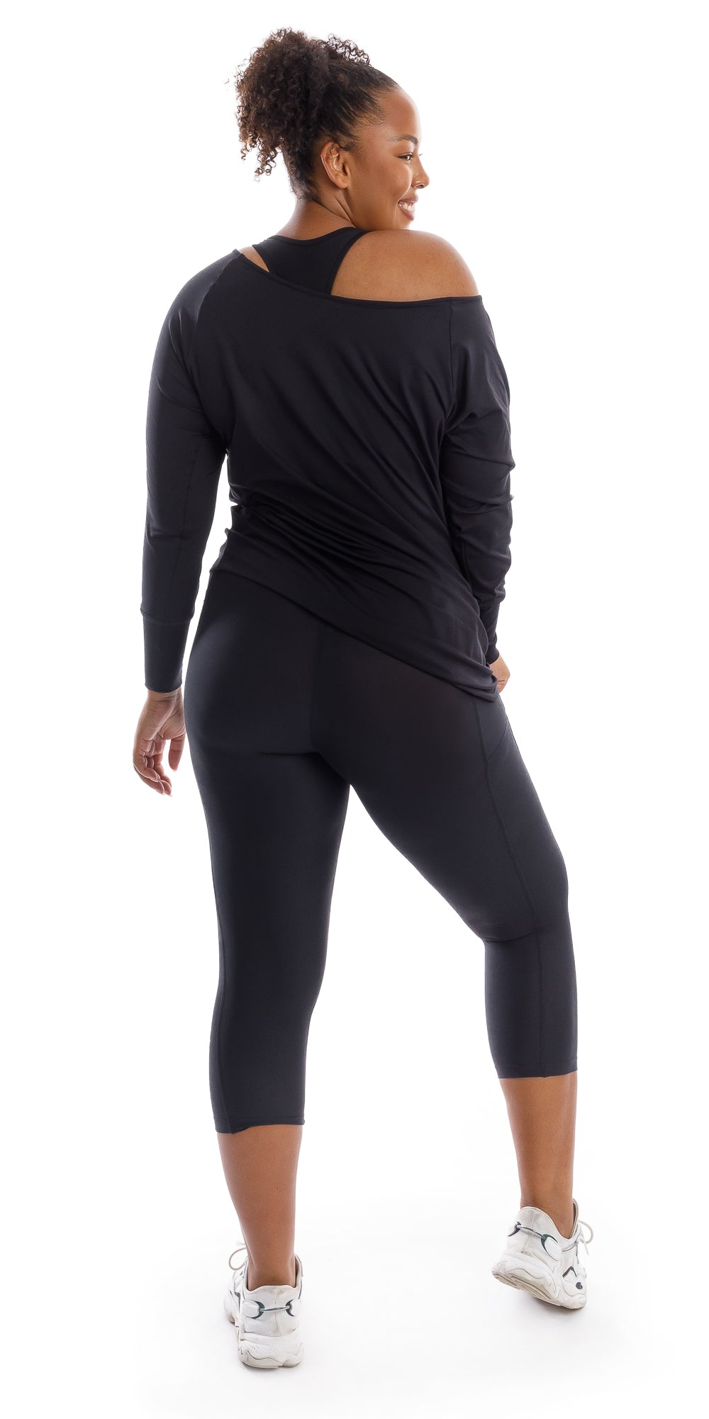 Full body rear view of girl wearing black Midnight Off The Shoulder Long Sleeve Tee and matching bottoms looking to her right and putting one leg forward