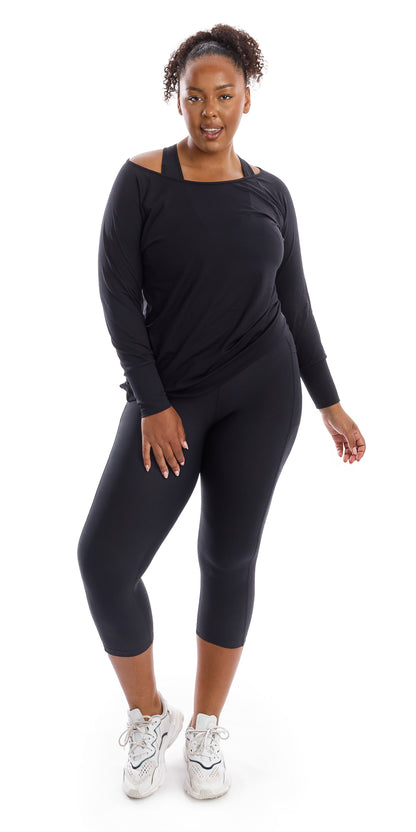 Full body front view of girl wearing black Midnight Off The Shoulder Long Sleeve Tee and matching leggings lifting one heel