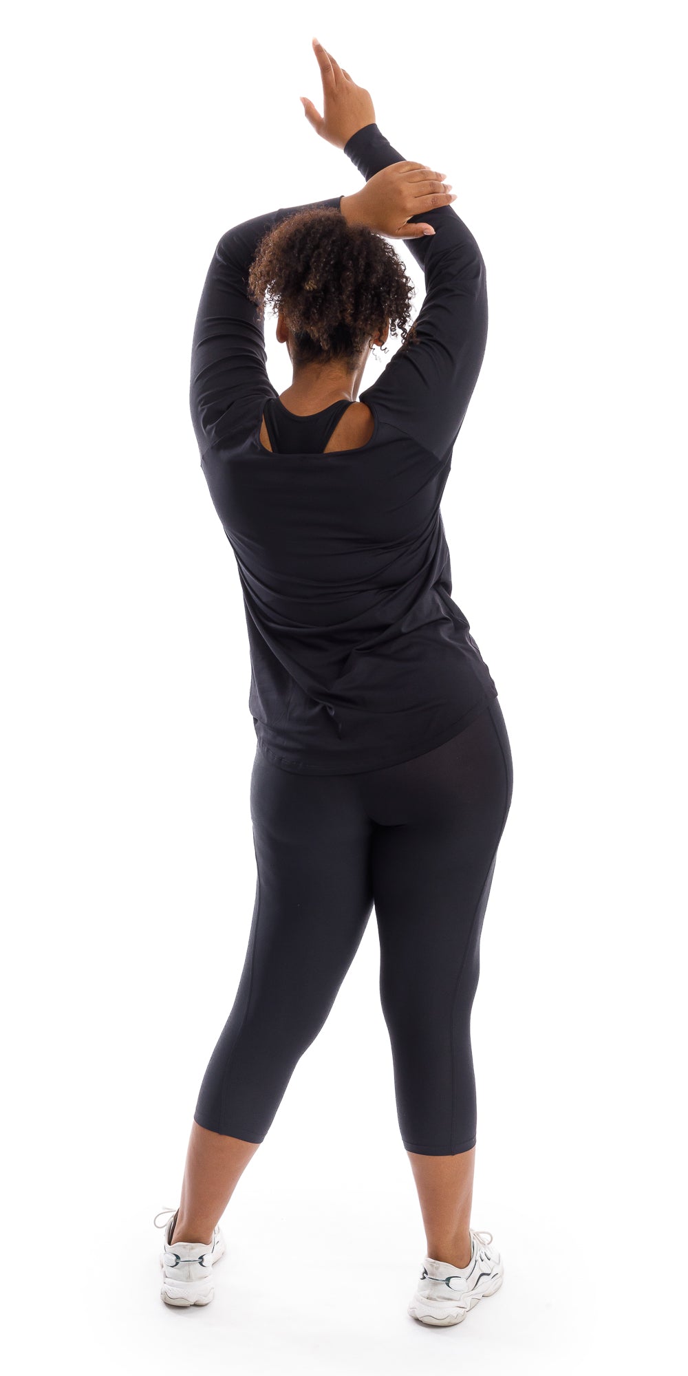 Full body rear view of girl wearing black Midnight Off The Shoulder Long Sleeve Tee and matching leggings lifting both arms towards the top of her head