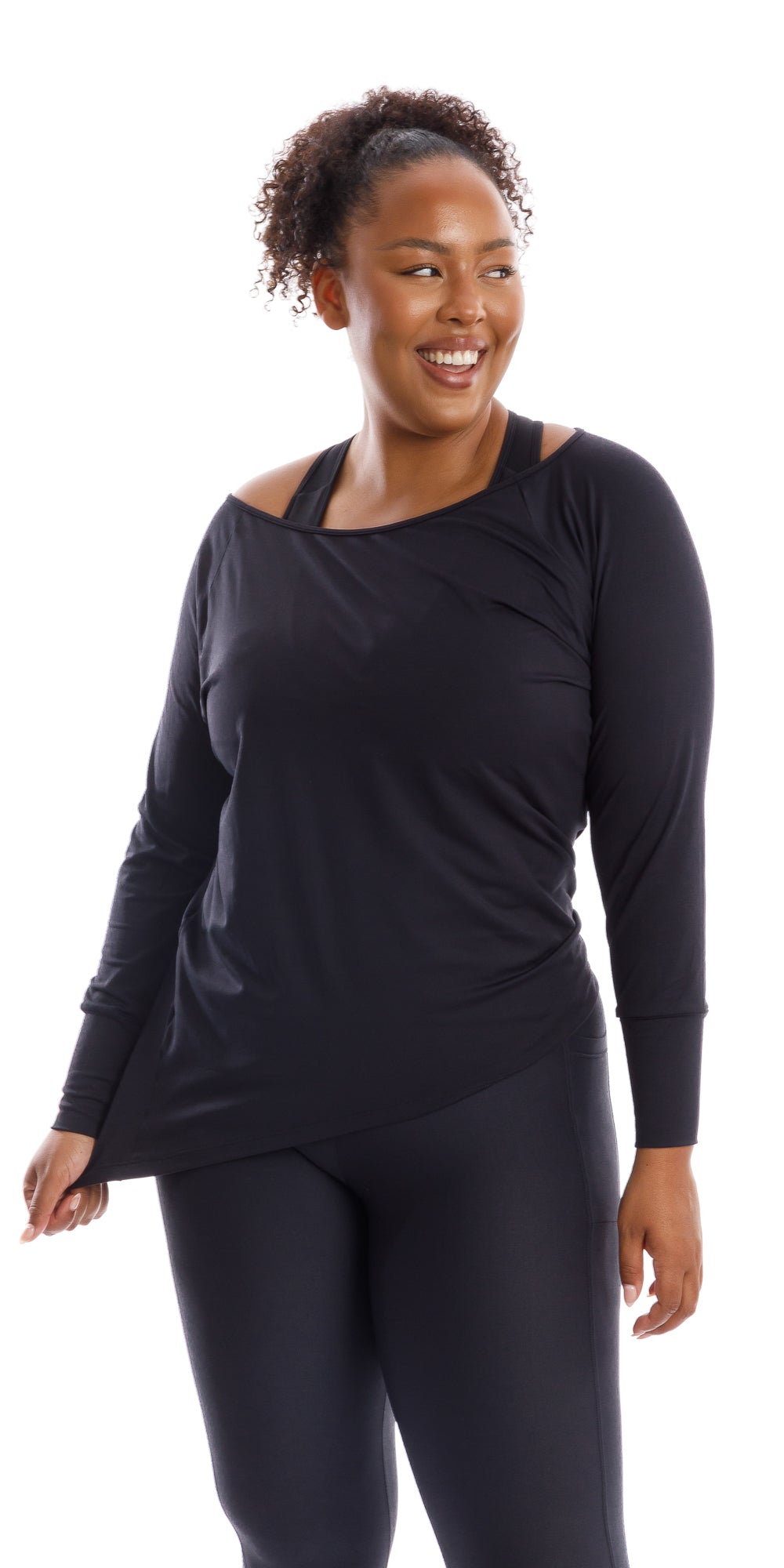 Front view of smiling girl wearing black Midnight Off The Shoulder Long Sleeve Tee and matching bottoms holding the end of her shirt