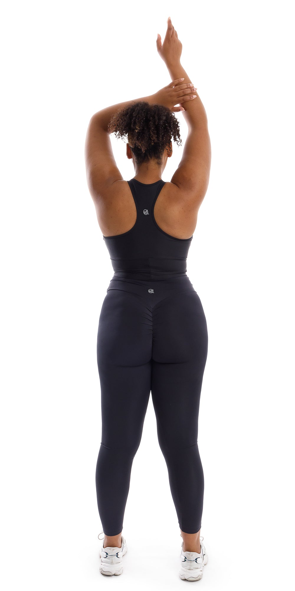 Full body rear view of girl in black Midnight Body Luxe Scrunch Bum Leggings and matching bra lifting one arm all the way up and folding the other