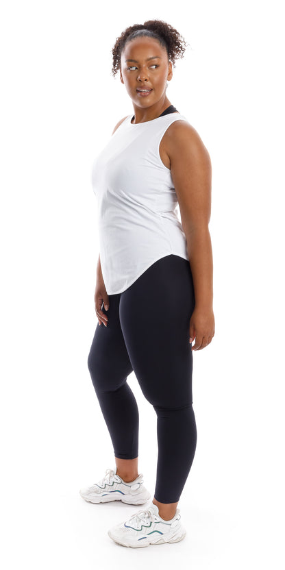 Full body left side view of lady in sleeveless White Palm Beach Tank and black leggings leaning on left leg bending the knee of the other while looking aside