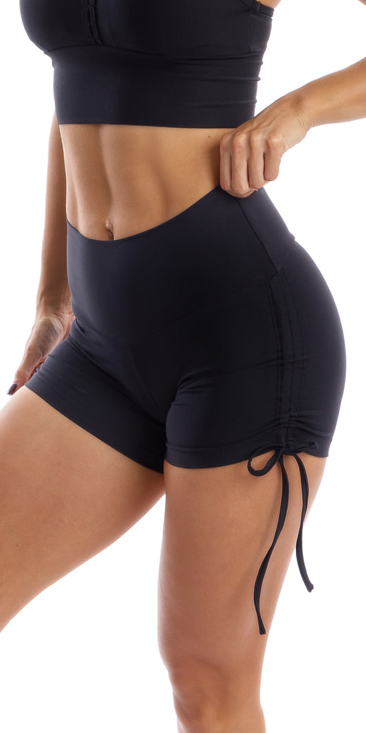 Side view of girl wearing black Midnight Eco Bootie Shorts with one hand pulling the shorts from the waist