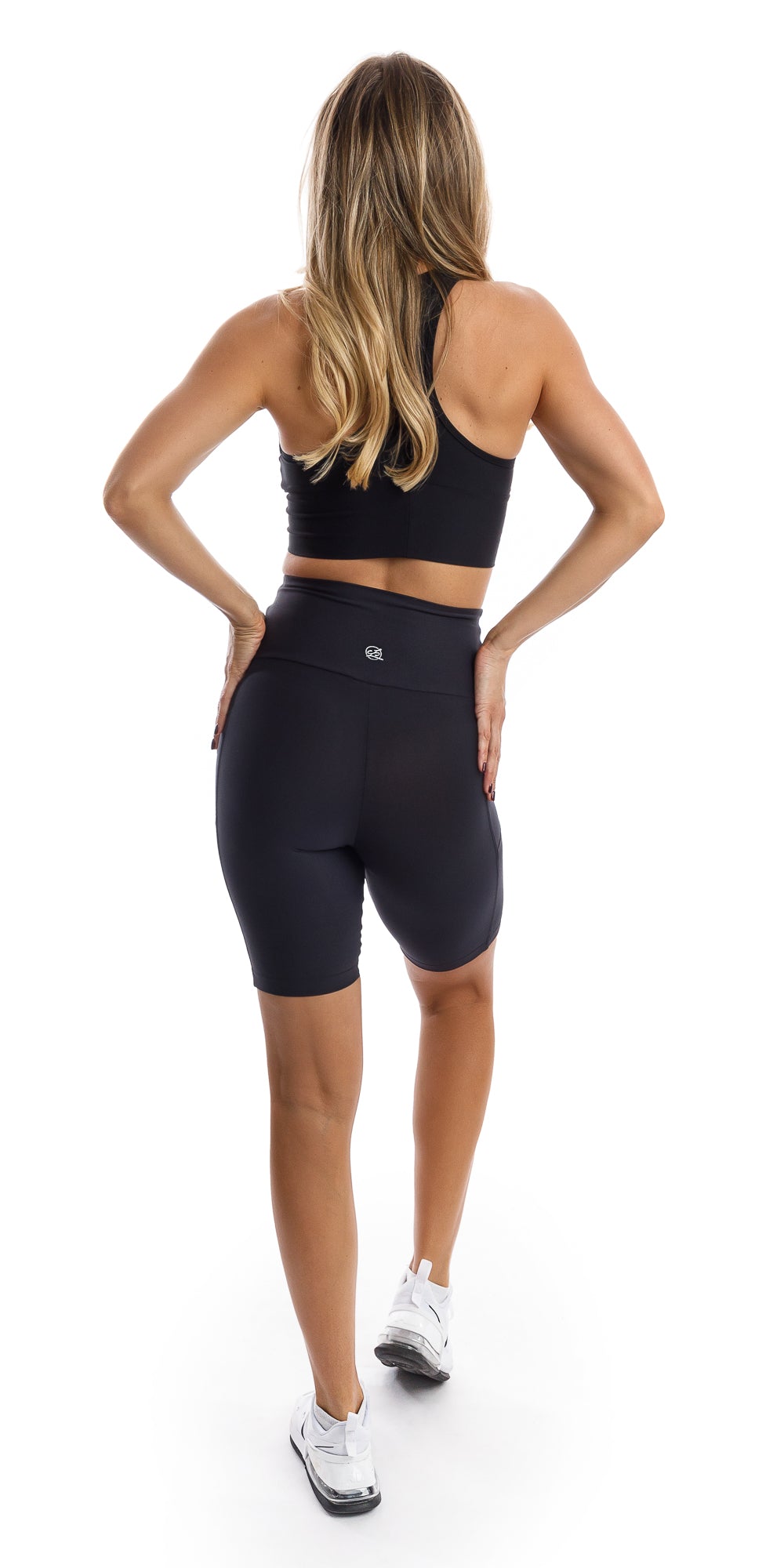 Full body rear view of girl in black Midnight Eco Biker Shorts with Pockets and matching bra putting both hands on waist
