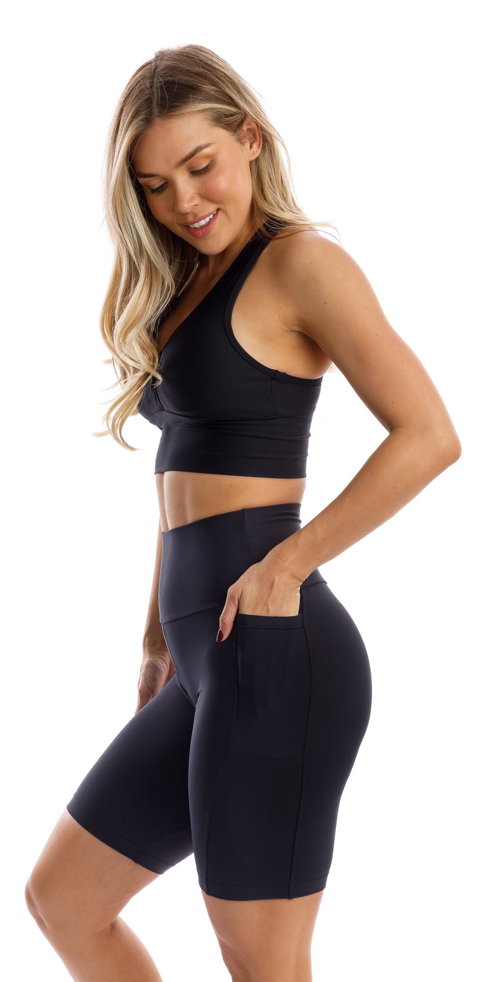Full body side view of girl in black Midnight Eco Biker Shorts with Pockets and matching bra putting one hand in the pocket