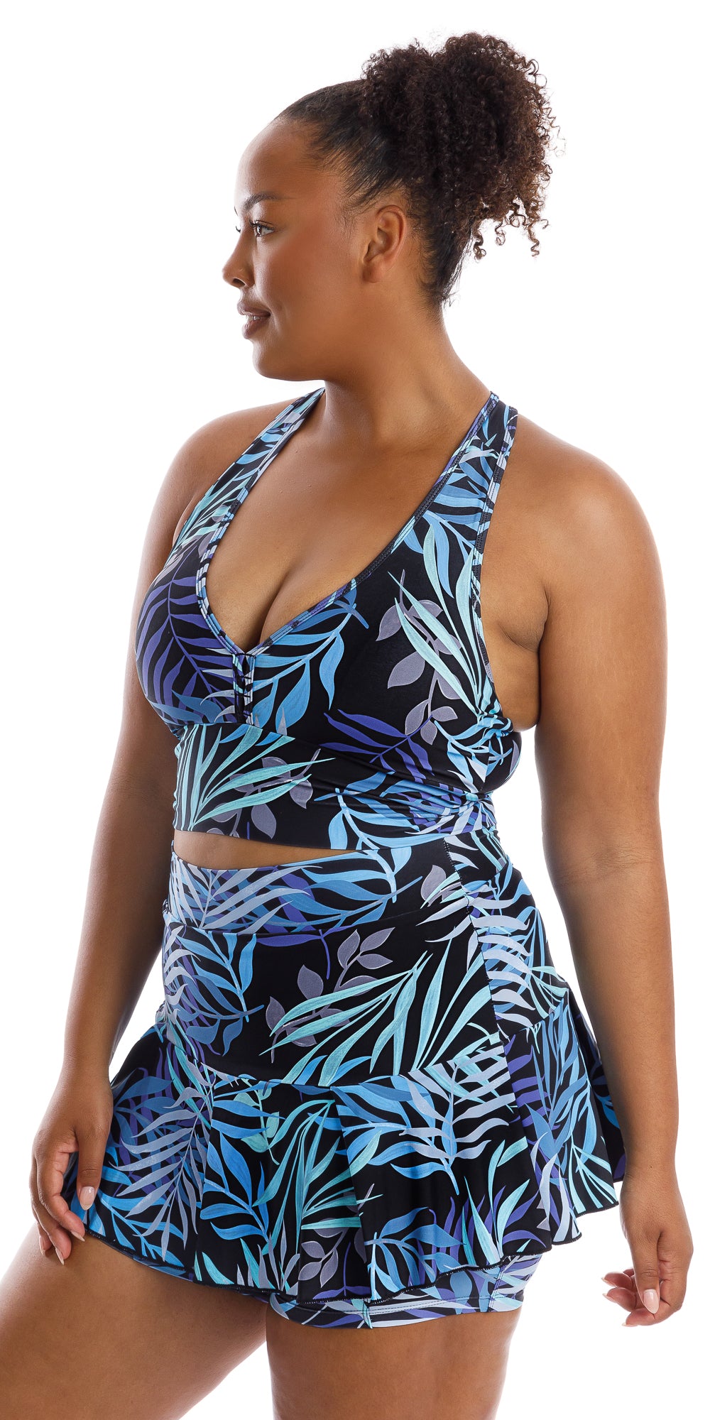 Angled front view of lady in black and blue Tropical Palm Skort with Pockets and matching bra putting one hand on lap while turning head to her right