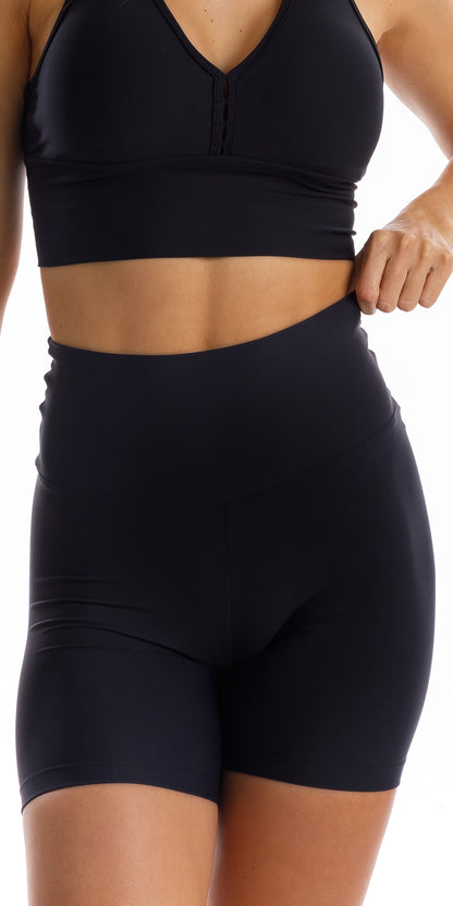 Front view of girl wearing black Midnight Eco Scrunch Bum Midi Shorts pulling waistband up