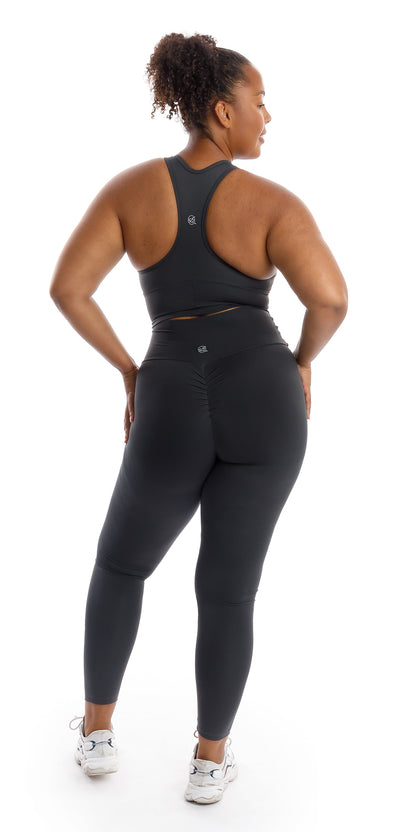 Full body rear view of girl wearing grey Liquorice Body Luxe Scrunch Bum Leggings and matching racer back bra putting both hands on waist