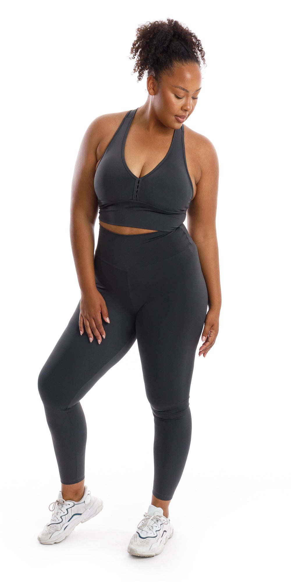 Full body front view of girl wearing grey Liquorice Body Luxe Scrunch Bum Leggings and matching racer back bra lifting one heel and looking down to her left