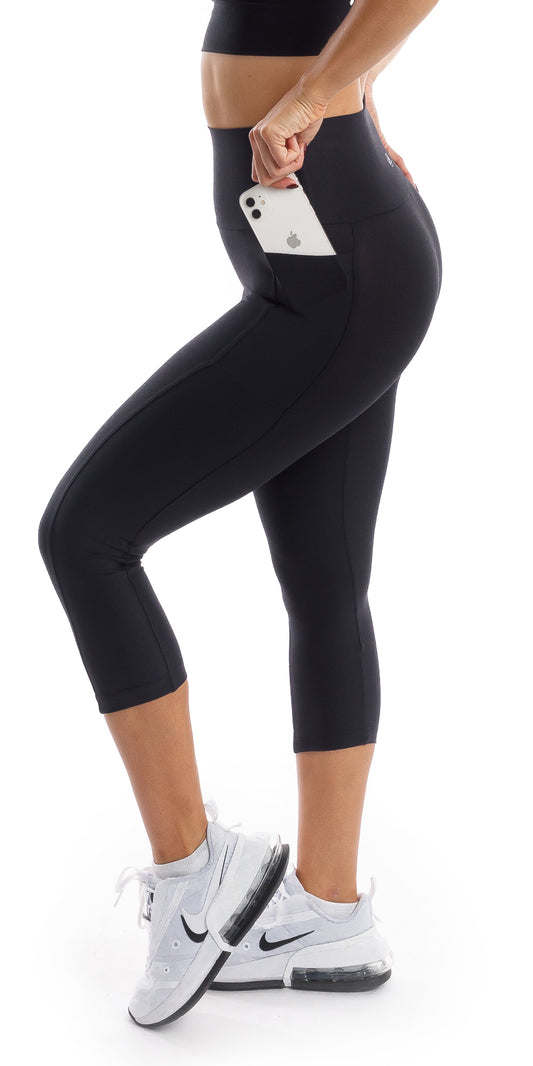 Side view of girl wearing black Midnight Eco Capri Leggings with Pockets putting phone in the pocket