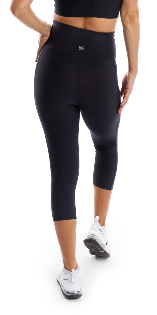 Rear view of girl wearing black Midnight Eco Capri Leggings with Pockets putting one hand on waist