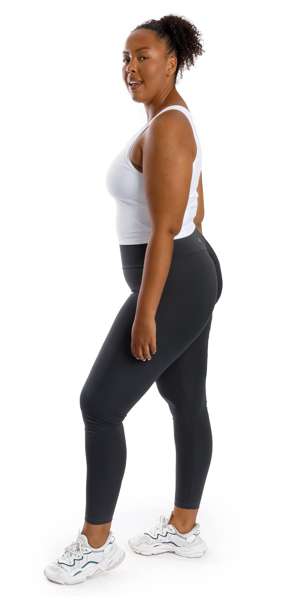 Full body side view of lady in sleeveless White Crop Top and black leggings putting left foot forward and looking to her left
