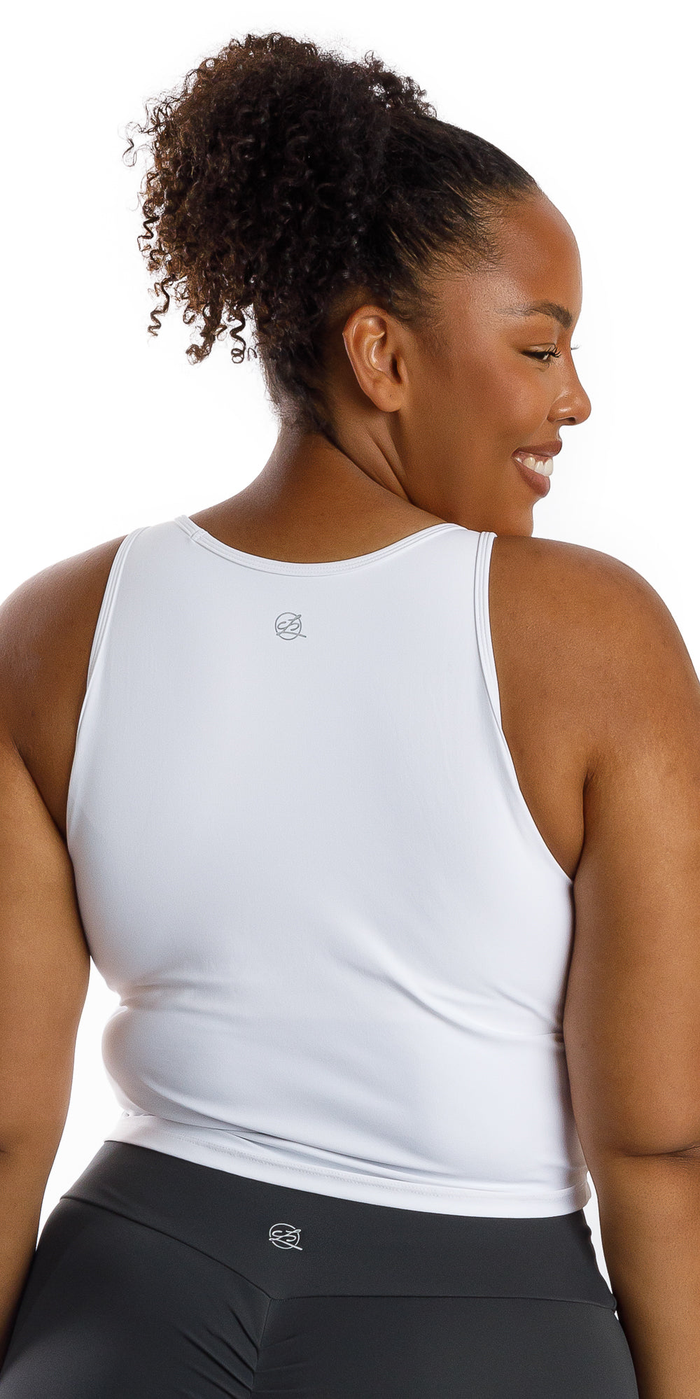 Back view of lady in sleeveless White Crop Top looking over right shoulder and smiling