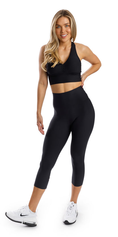 Full body front view of girl in black Midnight Eco Capri Leggings and matching bra putting one hand on waist