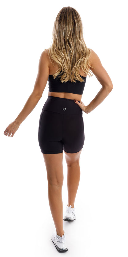 Full body rear view of girl in black Midnight Eco Midi Shorts with Pockets and matching bra putting one hand on waist