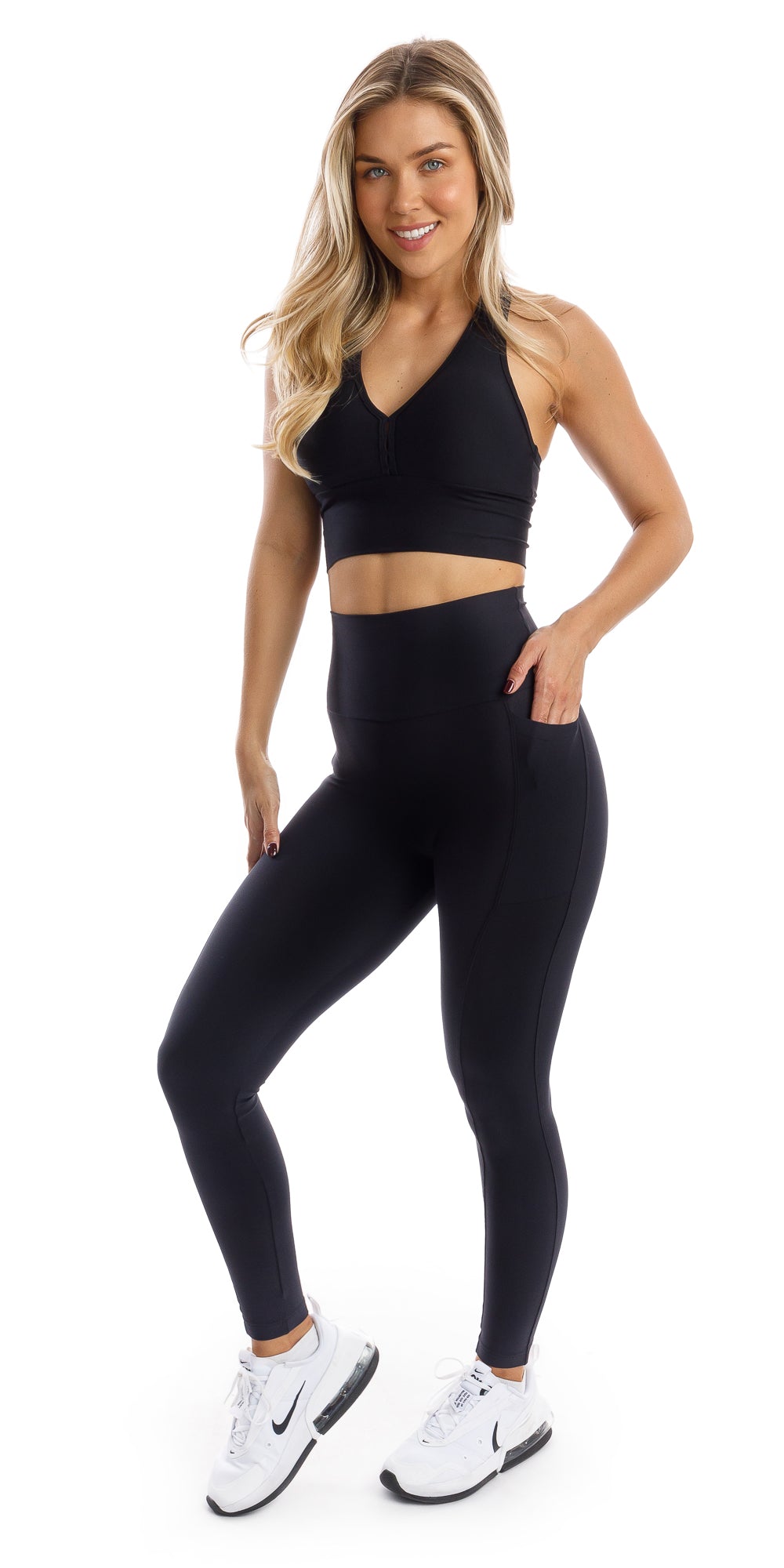 Full body front view of girl wearing black Midnight Eco Ultra High Waist Leggings with Pockets and matching bra putting one hand in the pocket