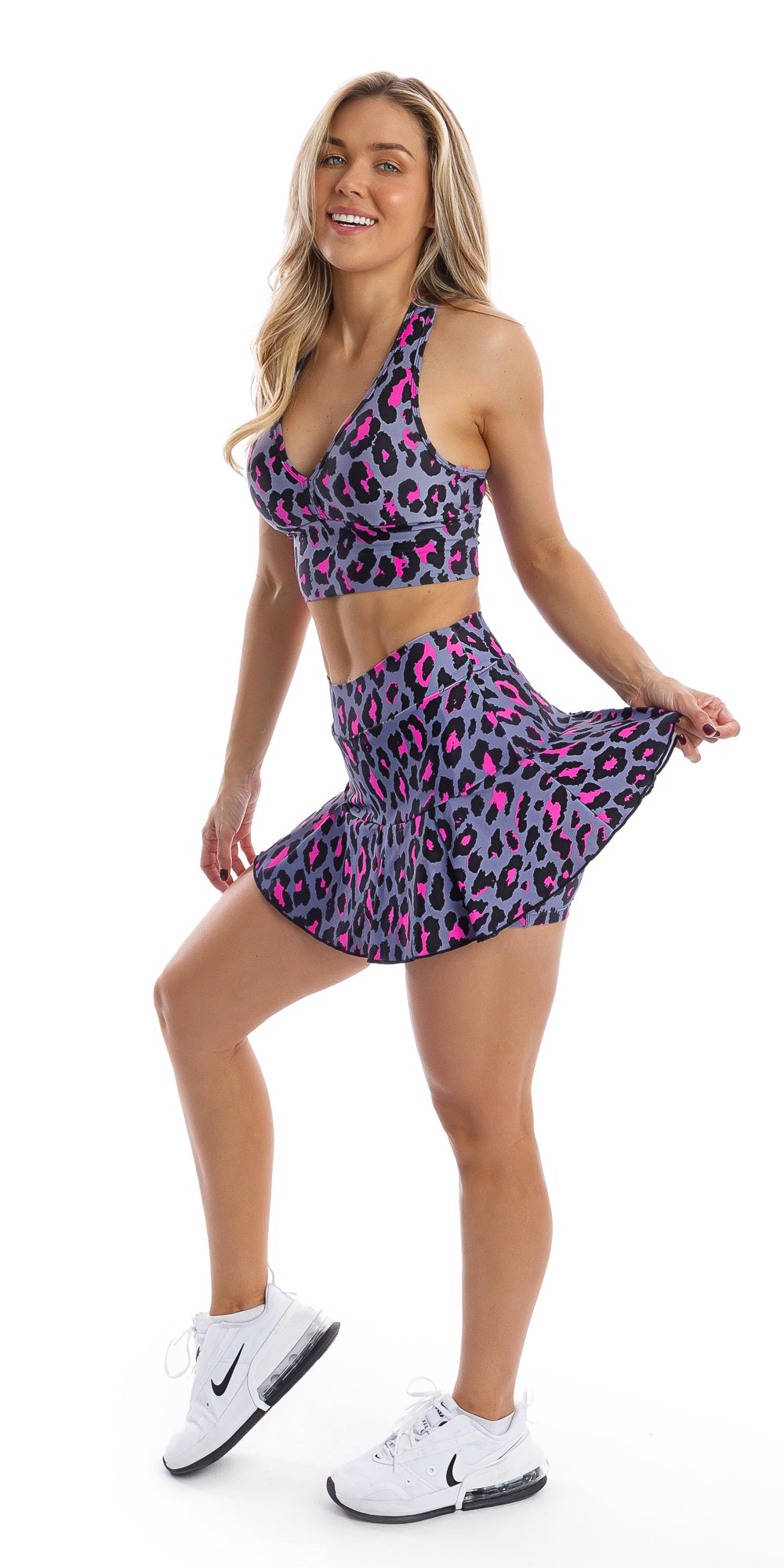 Full body front view of girl in animal print Pink Leopard Skort with Pockets and matching bra lifting right heel and pulling one side of the skort
