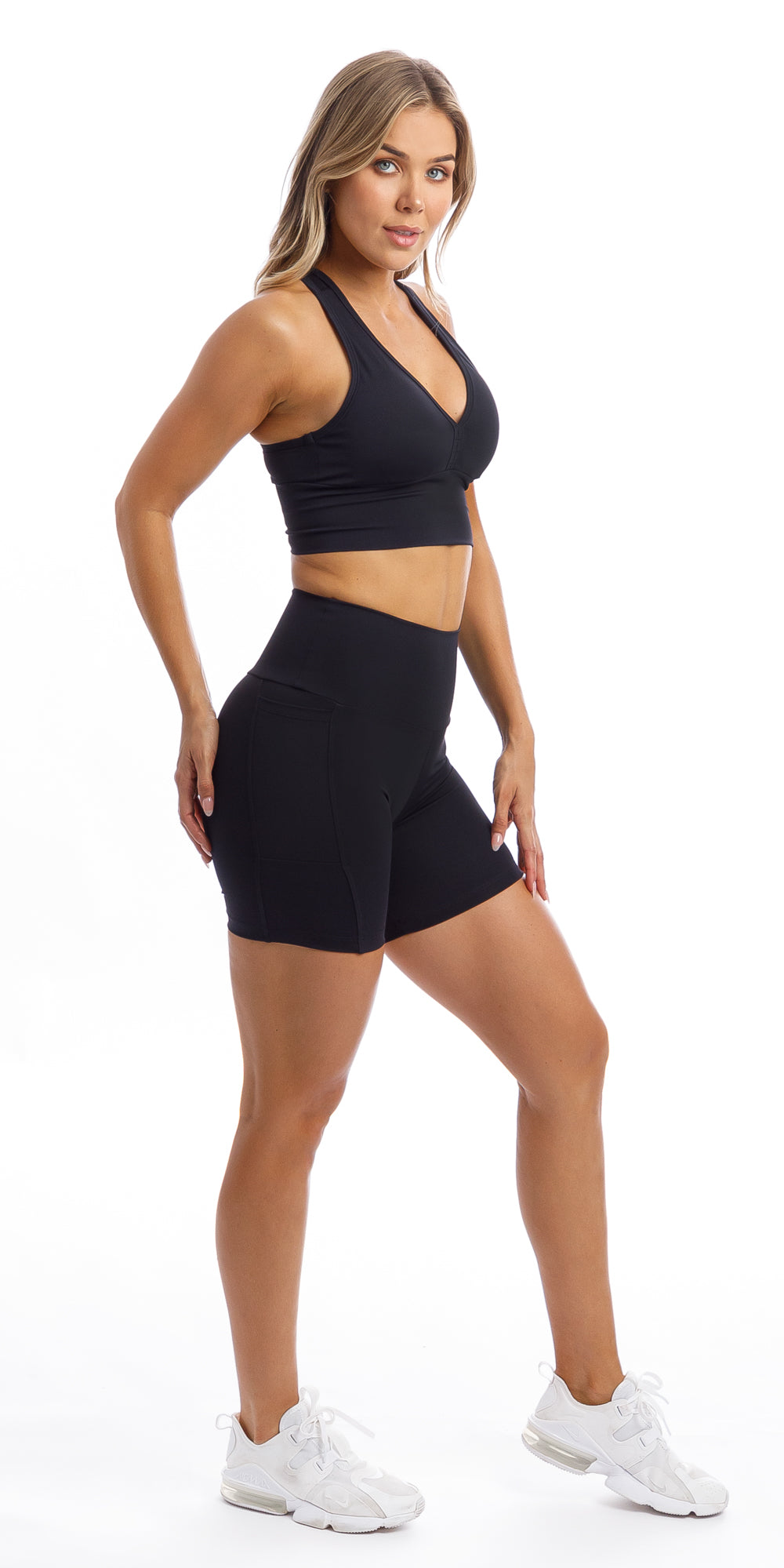 Side view of girl wearing midnight body luxe midi shorts with pockets & matching racer bra