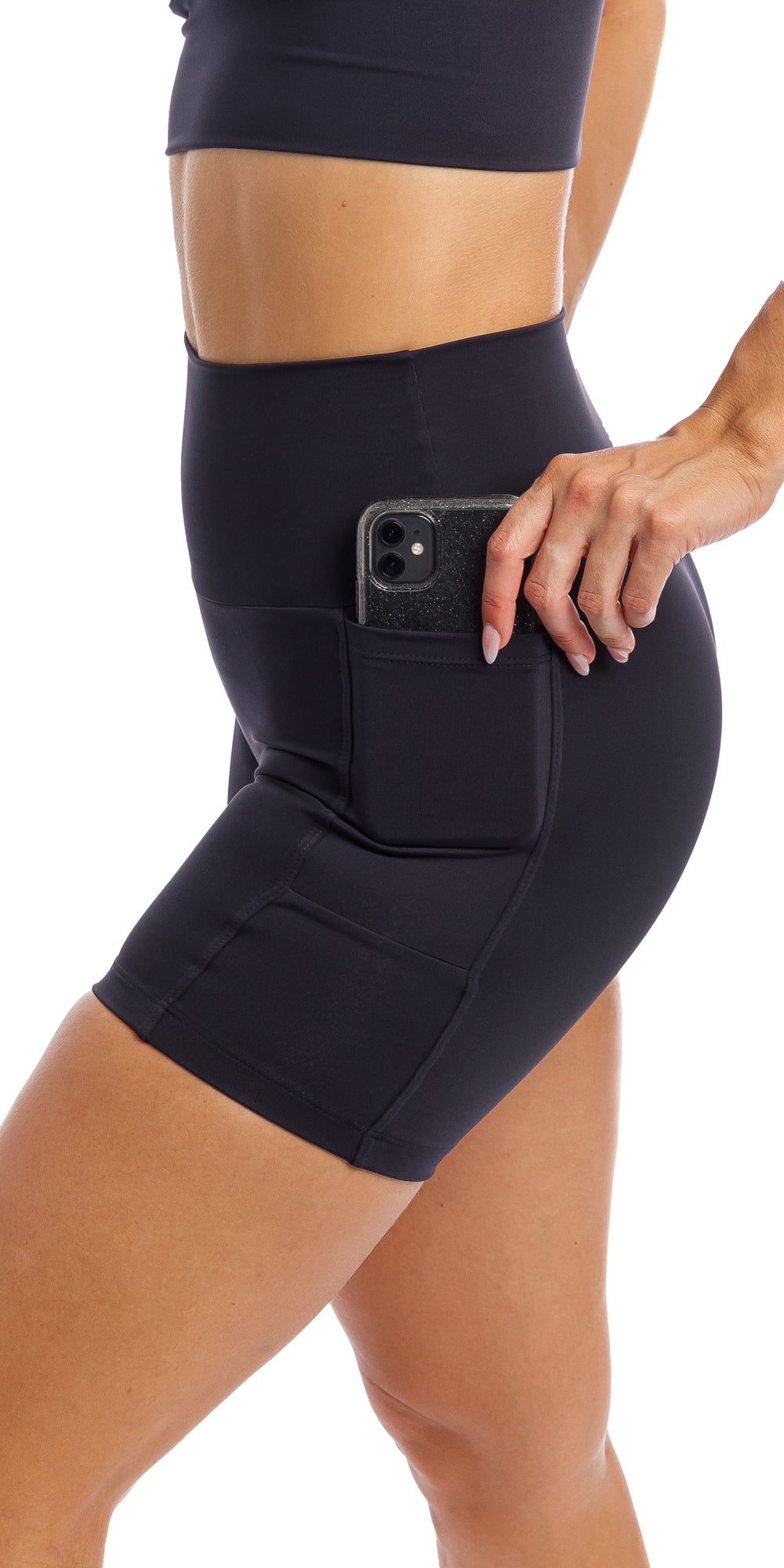 Girl putting phone in side pocket of midnight body luxe midi shorts with pockets & matching racer bra