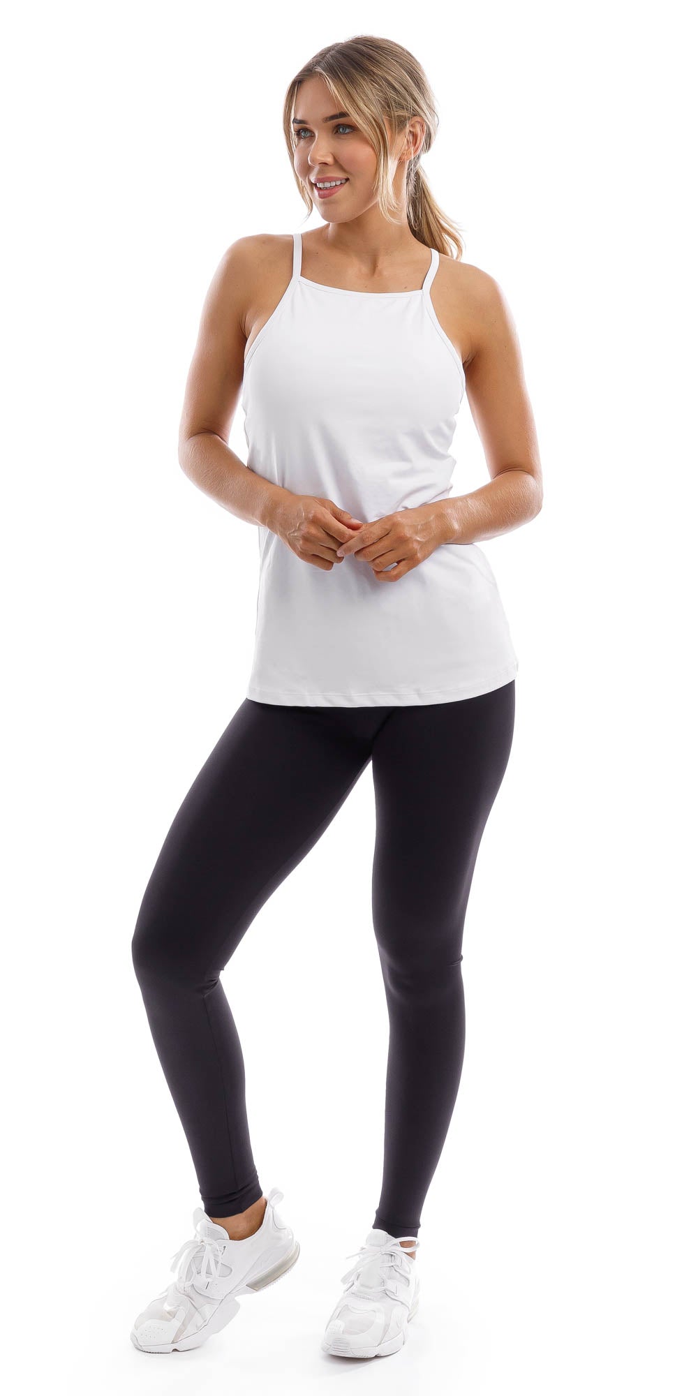 Full body front view of lady in strappy White Performance Tank and black leggings lifting right heel and putting hands together while looking aside
