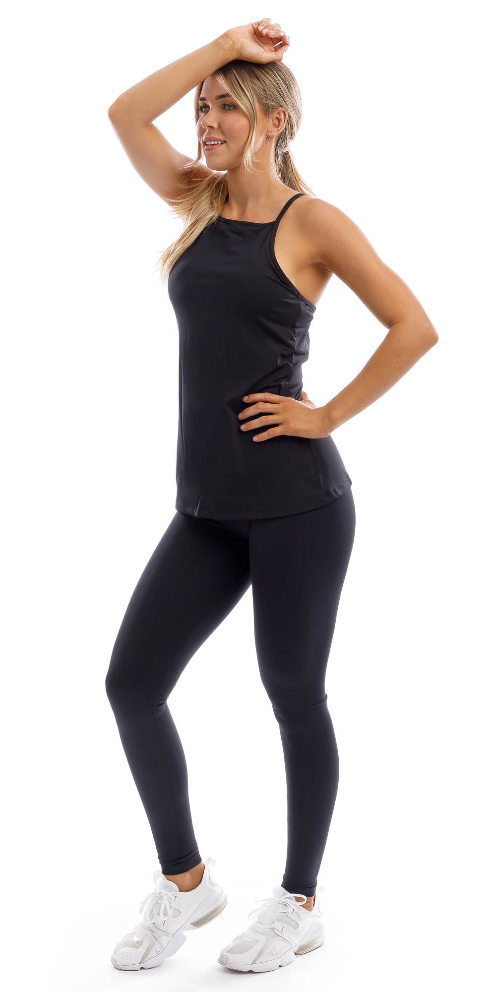 Full body angled side view of girl in black Midnight Performance Tank and matching leggings putting one leg forward, one hand on her head and the other hand on waist