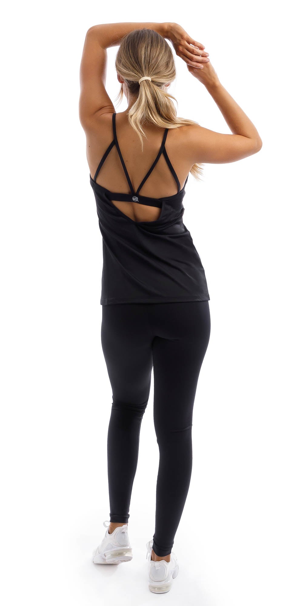 Full body rear view of girl in black Midnight Performance Tank and matching leggings putting one leg forward, both hands together over her head