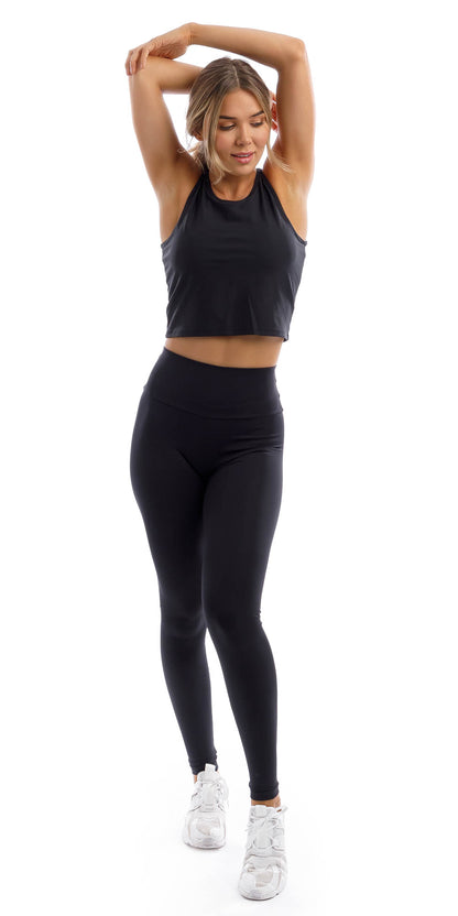 Full body front view of girl wearing black Midnight Crop Top and matching leggings putting both hands on top of her head