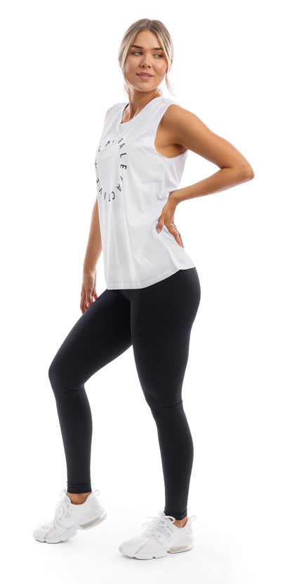 Full body angled front to side view of lady in White CL Active Tank and black leggings putting right foot forward and left hand on waist while looking aside
