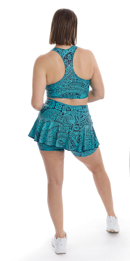Full body rear view of girl in aqua blue Paisley Tide Eco Racer Back Bra and matching skort putting one leg forward