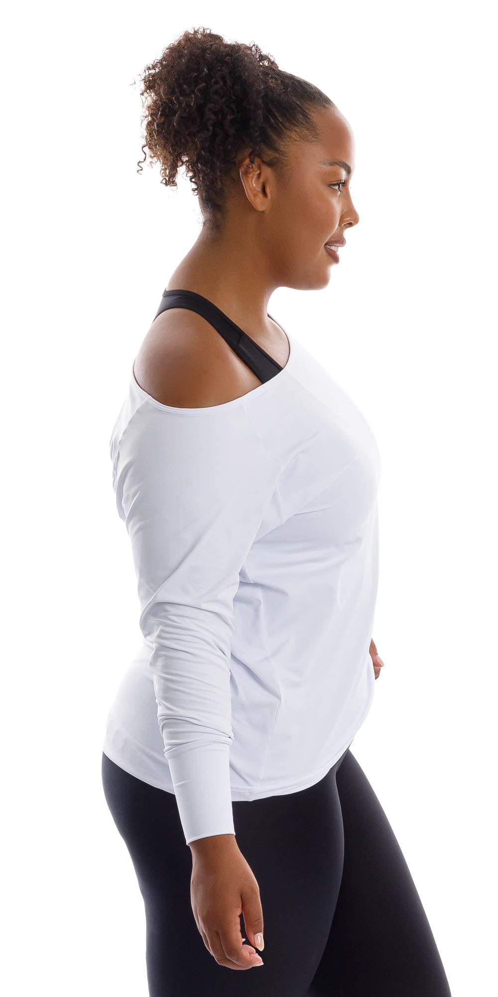 Side view of lady in White Off The Shoulder Long Sleeve Tee and black leggings putting left hand on waist and resting right arm