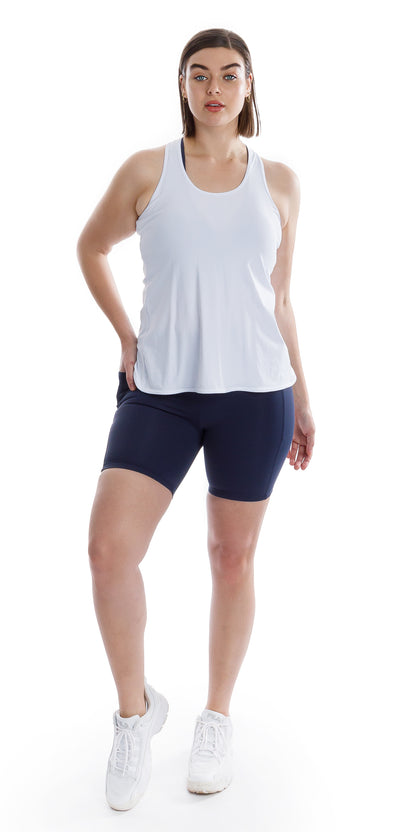 Full body front view of lady in sleeveless White Miami Tank and blue black bottoms putting right foot forward lifting its heel and putting right hand on waist