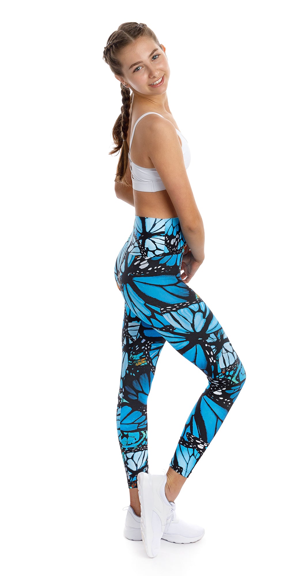 Full body side view of girl teenager in blue and black animal print Tween JH Butterfly Ultra High Waist 7/8 Leggings and white bra lifting right heel and putting left hand on waist while smiling for the camera