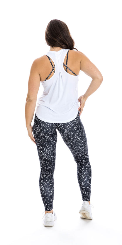 Full body rear view of lady in sleeveless White Meshed Racer Back Tank and black dotted leggings putting right foot forward lifting its heel and putting right hand on waist